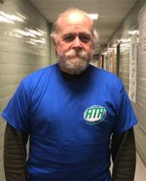 A man in blue shirt standing next to wall.