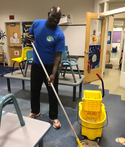 A man in blue shirt holding mop near yellow bucket.